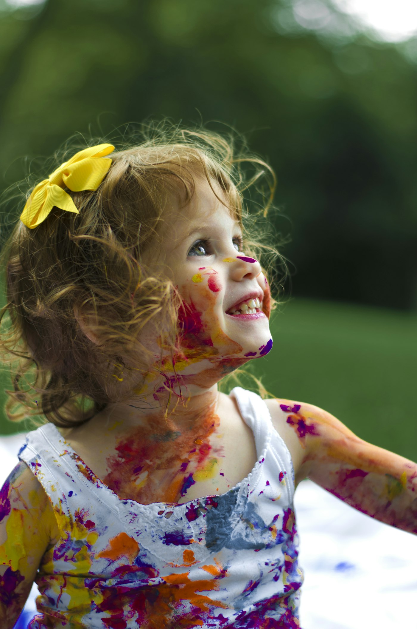 Little girl laughing outdoors with colourful paint covering her hands and face